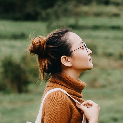 Perfil lateral de una mujer con un jersey de cuello alto de color rojizo y un bolso blanco. Mira hacia arriba con los ojos cerrados.